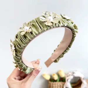 Close-up of elegant green pleated satin headband with gold metal flowers and pearls