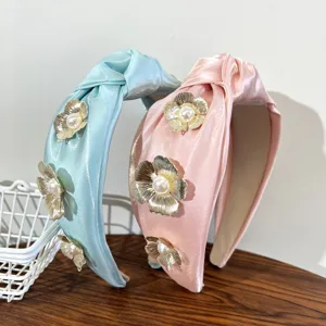 Detailed view of knotted satin headbands featuring 3D metallic flowers and pearls.