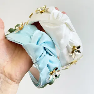 Gros plan sur des serre-têtes en satin noués avec fleurs 3D dorées et cristaux.