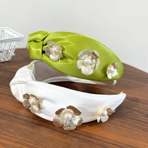 Detail view of elegant satin knotted headbands with gold metallic flowers and pearls.