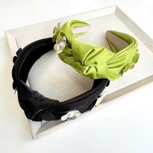 Detail view of knotted satin headbands featuring 3D metal flowers and pearl centers.