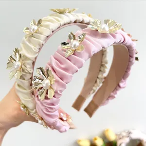 Close-up of elegant pleated satin headbands featuring gold metal flowers and pearls