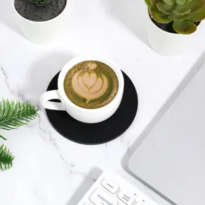 Top view of a black round felt coaster under a white coffee cup on a desk