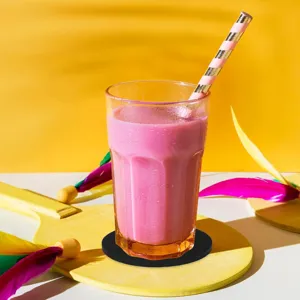 Macro view of a black round felt coaster under a glass of pink smoothie on a yellow background