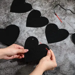 Detailed close-up showing the assembly process of a black felt heart garland with a needle