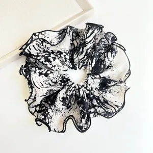 Detailed view of black and white tie-dye ruffled fabric scrunchie with ink splash pattern