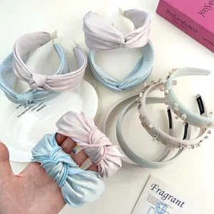 Detail van geknoopte stoffen haarbanden en kralen haarringen in pastelblauw en roze.