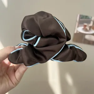 Detail view of coffee brown fabric hair scrunchie with light blue contrast piping