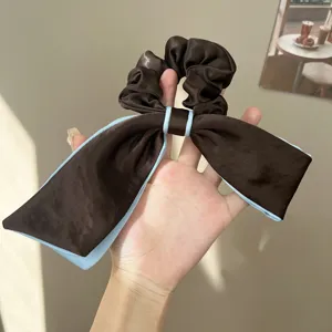 Detail view of an elegant brown satin bow scrunchie with light blue edges held in hand