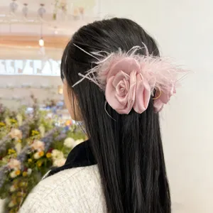 Detail view of a pink satin rose hair claw clip with elegant ostrich feathers.