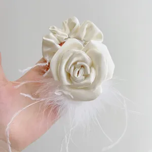 Close-up of elegant cream camellia satin scrunchie with white ostrich feathers.