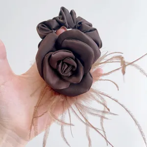 Detailed view of an elegant brown satin camellia rose scrunchie with soft ostrich feathers