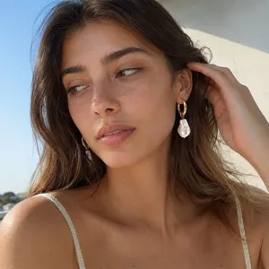 Close-up detail of elegant gold hoop earrings with baroque pearl drops on a model