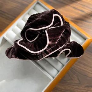 Macro detail view of a dark brown velvet scrunchie featuring elegant pink piping on jewelry tray