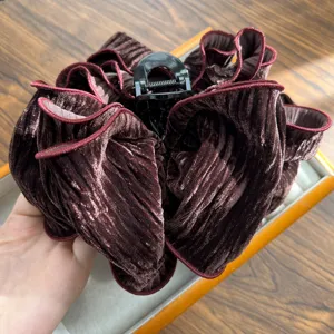 Macro view of a pleated burgundy velvet hair scrunchie with a black claw clip.