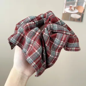 Λεπτομερής άποψη ενός vintage κόκκινου καρό scrunchie μαλλιών που κρατιέται στο χέρι.