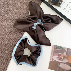 Detailed view of two elegant coffee brown silk scrunchies with light blue contrast edging.