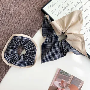 Close-up detail of navy blue plaid and beige fabric hair scrunchie with bow design