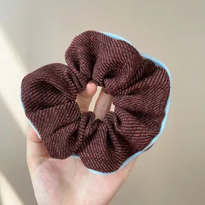 Detailed macro shot of a textured brown tweed scrunchie with elegant light blue piping
