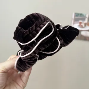 Detailed view of a brown velvet scrunchie held in hand with soft pink piping