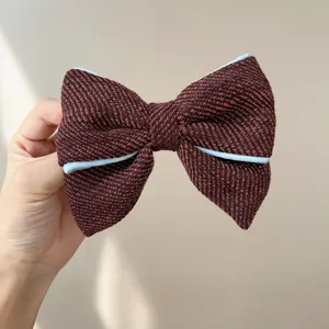 Detailed close-up of a burgundy tweed bow hair accessory with light blue piping detail.