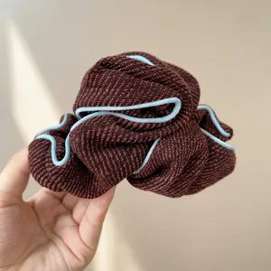 Detailed view of brown textured fabric scrunchie with light blue piped edging