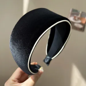 Close-up of an elegant black velvet padded headband with white piping and silver glitter