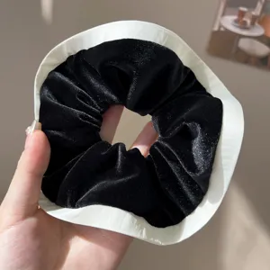 Close-up detail of a stylish black velvet scrunchie featuring a wide white fabric border