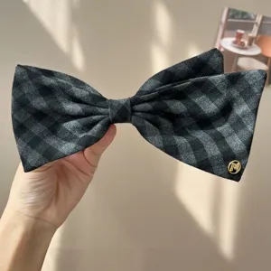 Close-up of a vintage grey plaid padded bow hair accessory featuring a golden M logo detail