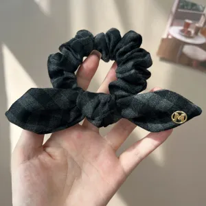 Close-up detail of a vintage dark grey plaid bow scrunchie with a gold metallic M logo charm