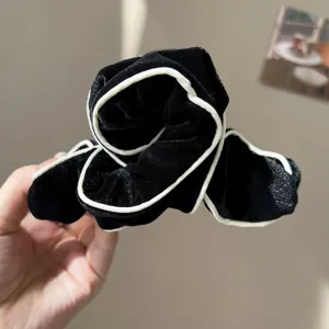 Close-up of black velvet hair claw clip with white contrast piping details.