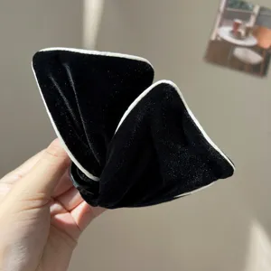Detailed close-up of an elegant black velvet bow hair clip featuring soft white piping accents