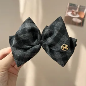 Close-up of vintage gray checkered bow hair clip with gold M detail