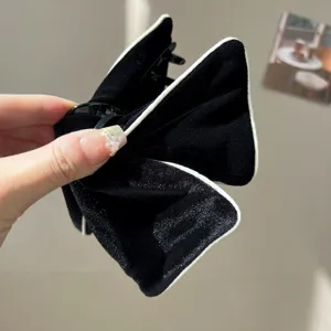 Close-up of elegant black velvet bow hair claw clip with white piping detail.