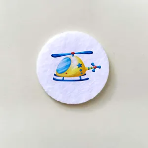 Detail view of a round white felt brooch with a colorful cartoon helicopter design