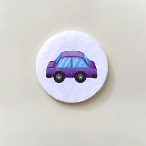 Macro detail view of a cute purple cartoon car badge on a soft white felt circle.