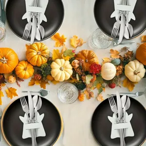 Close-up of white ghost-shaped cutlery holders on black plates for Halloween table decor.