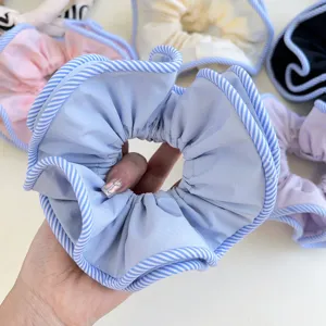 Close-up detail of a light blue fabric hair scrunchie featuring a striped piping edge design
