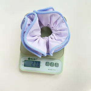 Detail view showing the weight of a large purple scrunchie with striped edges, 27.7g