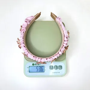 Close-up showing the 53.6g weight of the pink ruffled headband with floral accents.