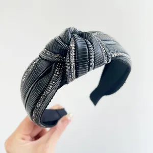 Primo piano di un cerchietto nero con nodo, decorato con strass lucenti e trame verticali