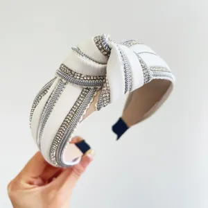 Dettaglio di fascia per capelli annodata bianca con strass luccicanti e treccia argentata.