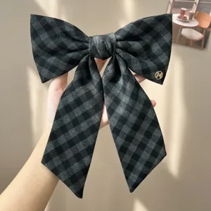 Detailed view of oversized grey checkered fabric bow hair clip with gold logo