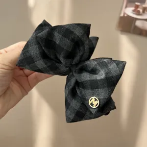 Detailed macro view of a vintage grey checkered bow hair clip featuring a gold M emblem
