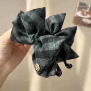 Close-up detail of a vintage grey checkered fabric bow hair grab clip with gold emblem