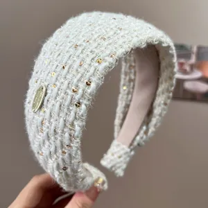 Detail of cream tweed headband with gold sequins and metal logo tag