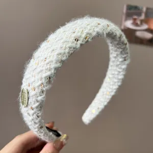 Close-up of white tweed knitted headband with gold sequins and metal logo
