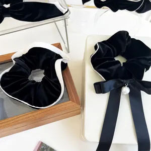 Close-up of black velvet scrunchies with white piping and elegant ribbon bow detail.