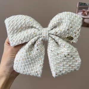 Detailed macro shot of a cream tweed bow hair clip decorated with shiny gold sequins