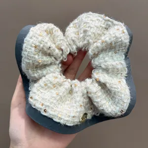 Detailed macro view of cream tweed scrunchie with golden sequins and elegant gray border